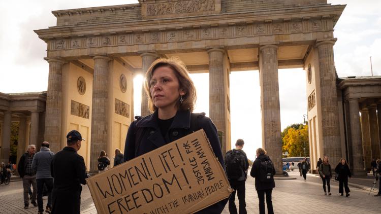 Anikó vor dem Brandenburger Tor in Berlin auf dem Weg zur Demo in Solidarität mit den AktivistInnen im Iran. In der Hand hält sie ein Demonstrationsschild mit der Aufschrift "Women! Life! Freedom!"